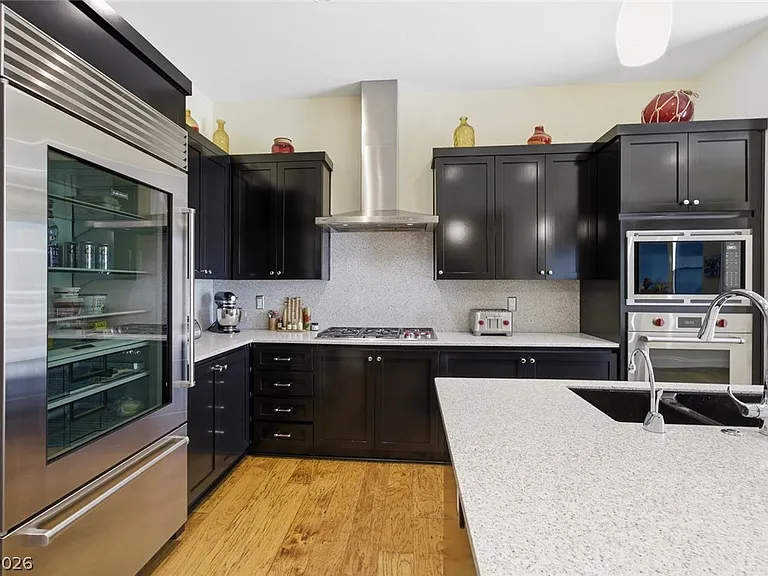 Wolf five-burner gas cooktop with stainless hood, Sub-Zero glass-door refrigerator on the left, and black shaker cabinetry framing the work zone
