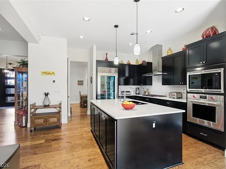 Kitchen wide angle showing black shaker cabinets, quartz center island with breakfast bar, pendant lighting, and engineered hardwood flooring