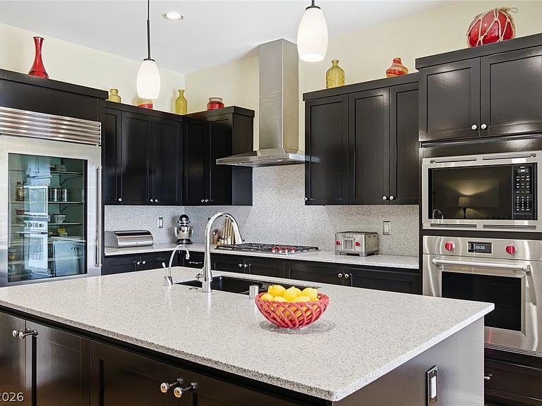Close angle of the kitchen island with a quartz countertop, pendant lighting overhead, and stainless wall ovens visible in the background